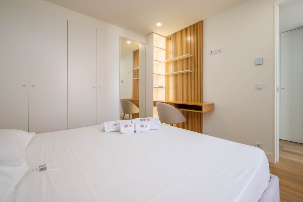 Quarto de casal com roupeiro branco e painel de ripado de madeira com secretária integrada, apartamento Home mg Matosinhos