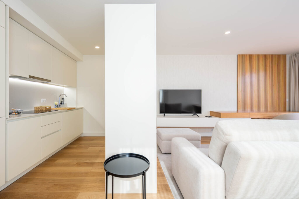 Vista da cozinha branca para a sala de estar com painel de ripado de madeira, apartamento de alojamento Matosinhos