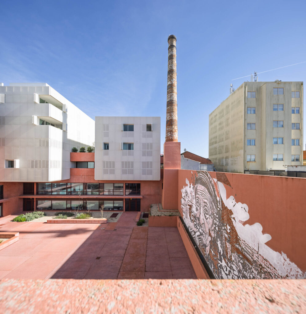 Vista do pátio interior da Antiga Fábrica de Conservas com chaminé industrial e mural urbano de grande dimensão
