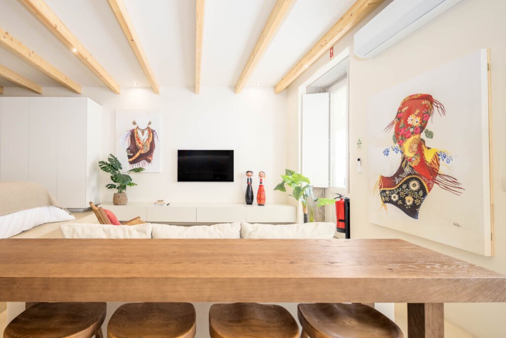 Vista a partir da mesa de madeira para a sala com televisão, figuras populares e telas de traje tradicional de Viana