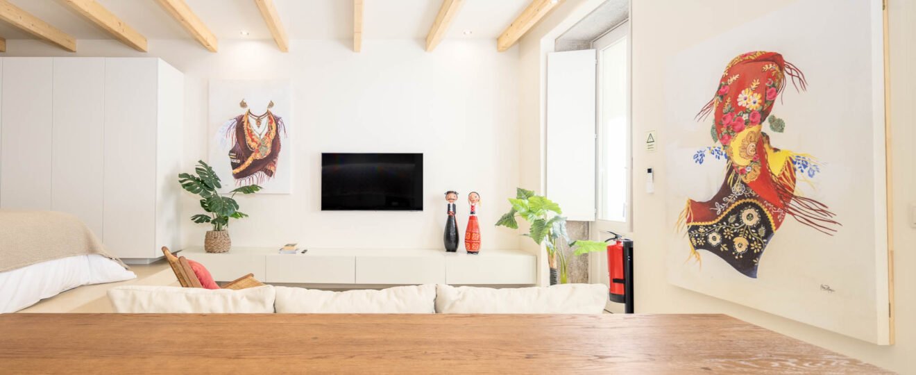 Vista a partir da mesa de madeira para a sala com televisão, figuras populares e telas de traje tradicional de Viana