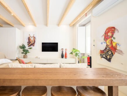 Vista a partir da mesa de madeira para a sala com televisão, figuras populares e telas de traje tradicional de Viana