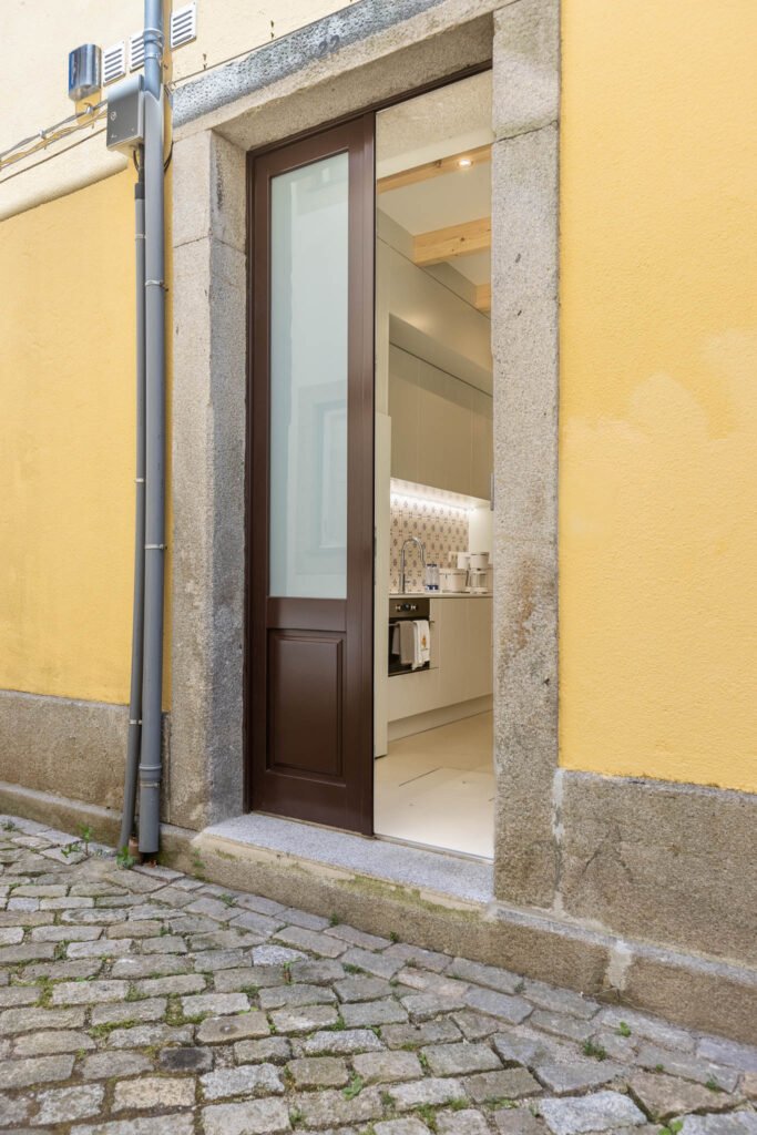 Porta entreaberta em moldura de pedra revela cozinha com azulejo azul, fotografia de interiores vista da rua