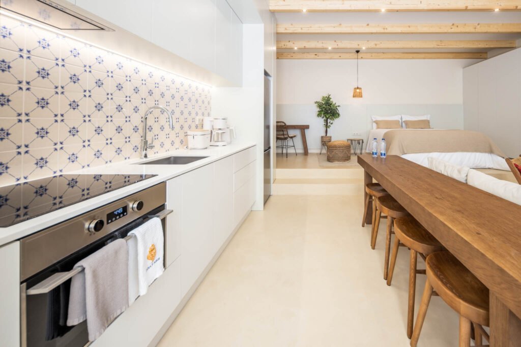 Cozinha linear com azulejo azul e branco iluminado, mesa de madeira e zona de dormir elevada ao fundo