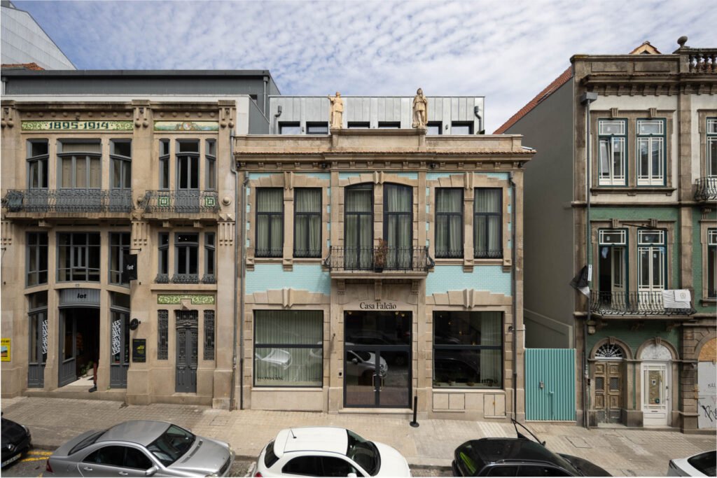 Fachada reabilitada de hotel boutique na Baixa do Porto, com pedra, azulejo azul-claro e duas estátuas, enquadrada entre os edifícios vizinhos