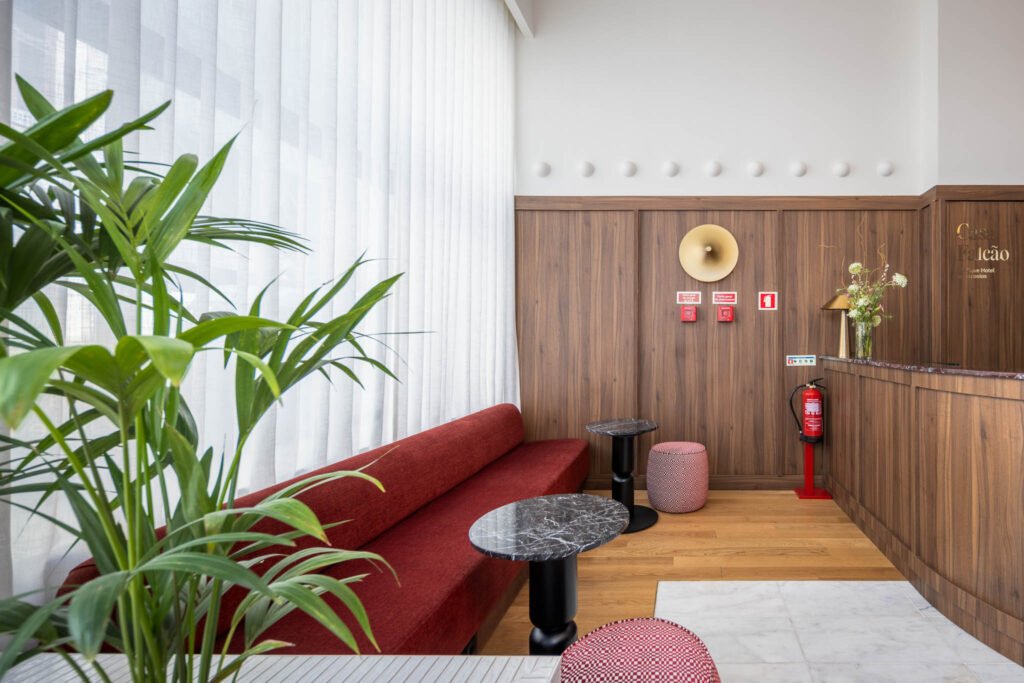 Canto junto à recepção de hotel boutique no Porto, com banco corrido vermelho, mesas de apoio escuras e revestimento em madeira