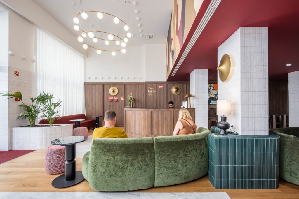 Fotografia de hotel boutique: recepção da Casa Falcão com hóspedes num sofá curvo verde, candeeiro circular de globos e tecto vermelho