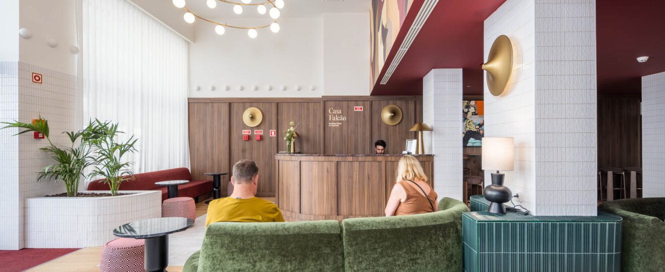 Fotografia de hotel boutique: recepção da Casa Falcão com hóspedes num sofá curvo verde, candeeiro circular de globos e tecto vermelho