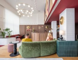 Fotografia de hotel boutique: recepção da Casa Falcão com hóspedes num sofá curvo verde, candeeiro circular de globos e tecto vermelho