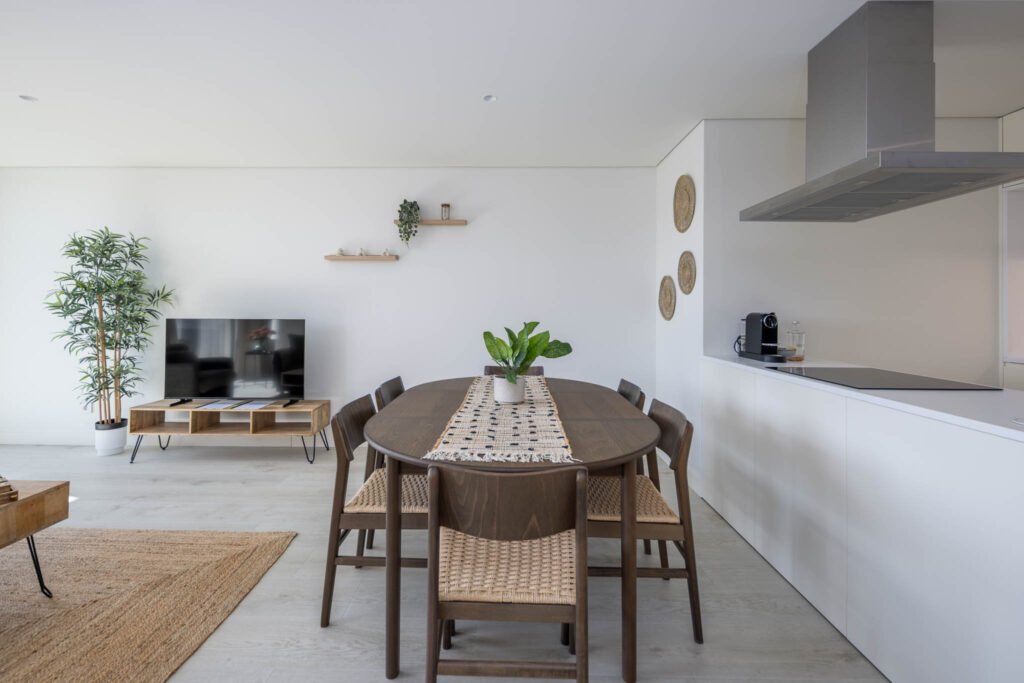 Zona de refeições com mesa em madeira escura e cozinha branca em open space