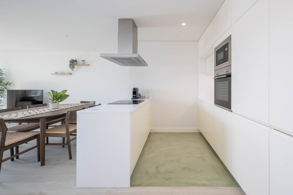 Cozinha branca com ilha, exaustor em inox e pavimento verde