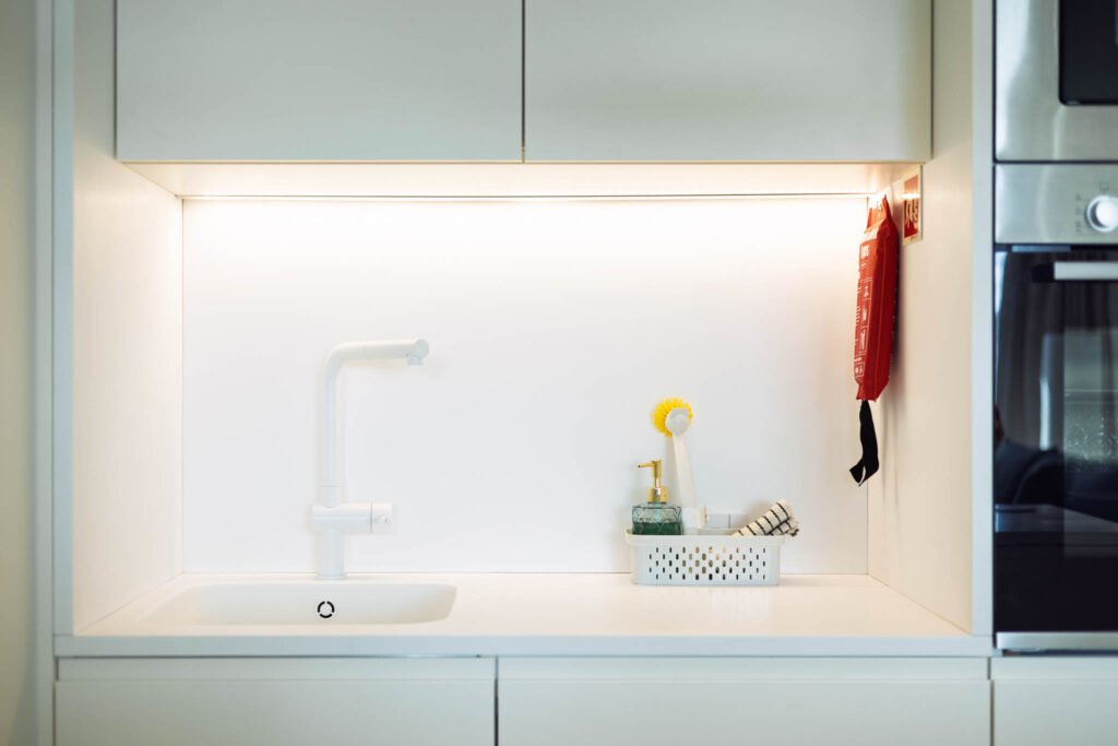 Bancada da cozinha com torneira branca e iluminação sob os armários