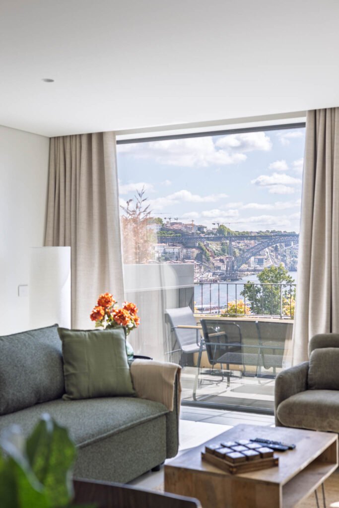 Sala com sofá verde e janela para a varanda, com vista para a Ponte Luís I